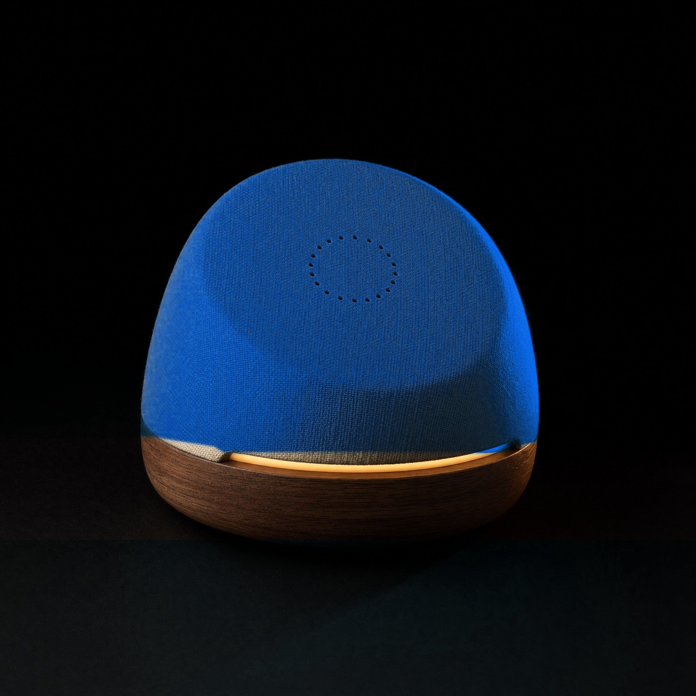 Hank concept: a soft tilted cobalt-blue fabric dome on a walnut base, its face turned toward the viewer, with a circle of microphone ports and a warm ochre light under the lip